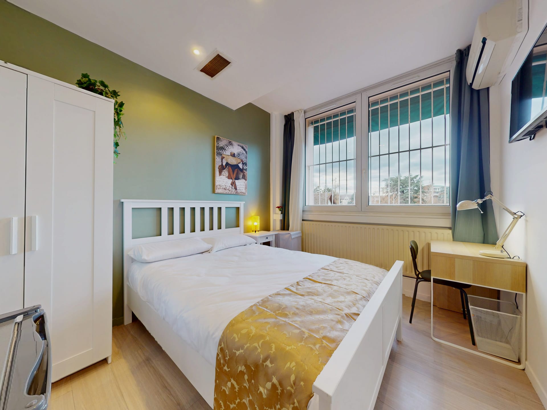 Chambre meublée avec bureau, chaise, télévision murale et climatisation