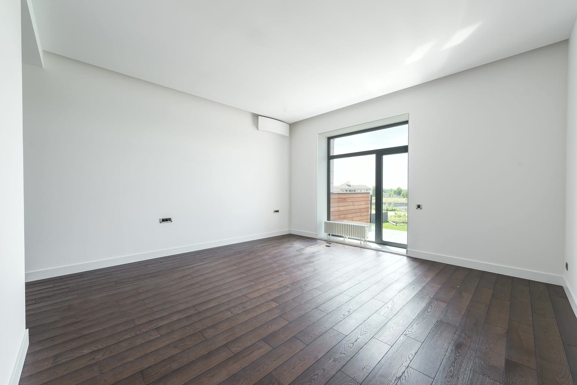 Pièce vide aux murs blancs et au parquet foncé, sans mobilier